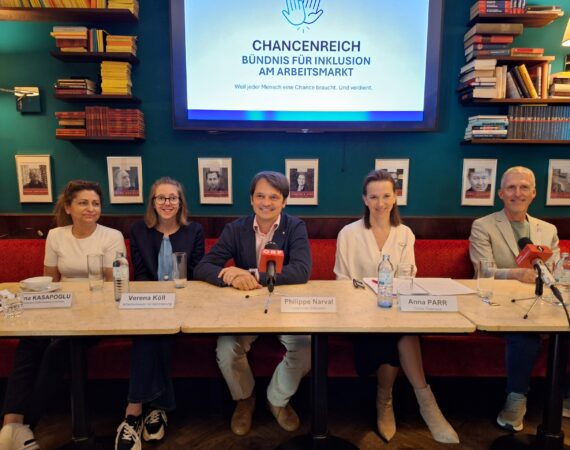 Fünf Personen sitzen an einem langen Tisch mit Mikrofonen und Wasserflaschen und lächeln bei einer Presseveranstaltung. Hinter ihnen ist ein Bildschirm mit dem Logo CHANCENREICH BÜNDNIS FÜR INKLUSION AM ARBEITSMARKT zu sehen.