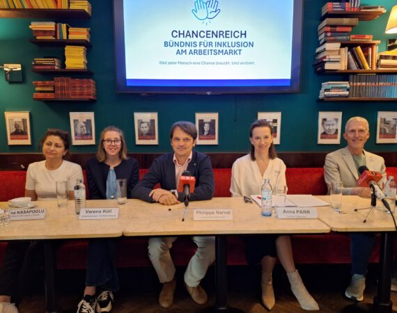 Fünf Personen sitzen an einem langen Tisch mit Mikrofonen und Wasserflaschen und lächeln bei einer Presseveranstaltung. Hinter ihnen ist ein Bildschirm mit dem Logo CHANCENREICH BÜNDNIS FÜR INKLUSION AM ARBEITSMARKT zu sehen.